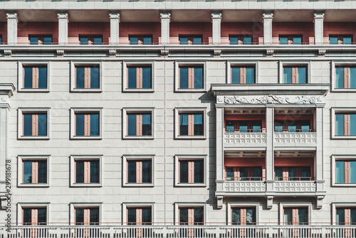 A grayish facade of a modern multi-storey building made in a typical modern Russian architecture style in Moscow: plenty of windows, balconies, bas-relief; a regular house frontage texture