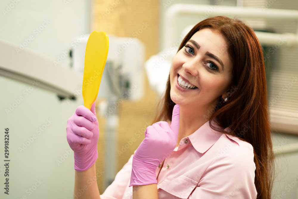 Beautiful female dentist shows healthy teeth. Smiling and holding a mirror. Dentistry and oral hygiene. Beautiful female dentist shows healthy teeth. Smiling and holding a mirror. Dentistry and oral hygiene.