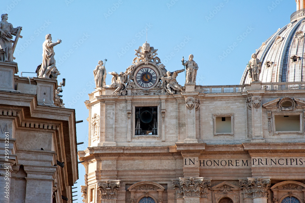 The top-left corner of the Basilica of St. Peter in the Vatican with the clock and the belfry. The standing statues are Saints Thaddeus (left) & Matthew (right).