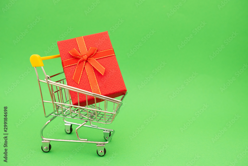 Annual sale shopping season concept - mini shopping cart trolley with gift isolated on green background, empty copy space, close up