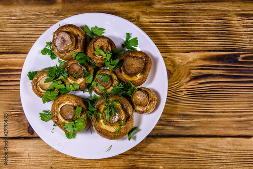 Plate with baked champignons, dill and parsley on a wooden table. Top view