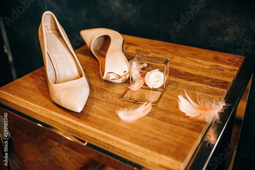 Wedding accessories for a luxurious wedding day. Beige shoes and wedding ring on wooden table