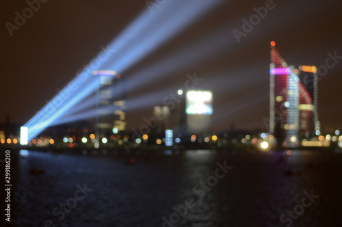 long exposure, blurred background, night view of the city center and the river bay with festive lights, searchlight blue beams, a business center tower, night city life