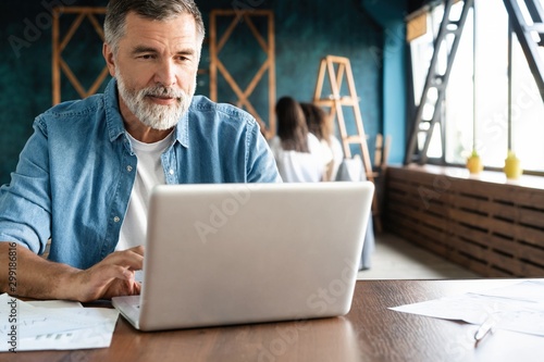 Cheerful mature man working on laptop and smiling while sitting at his working place