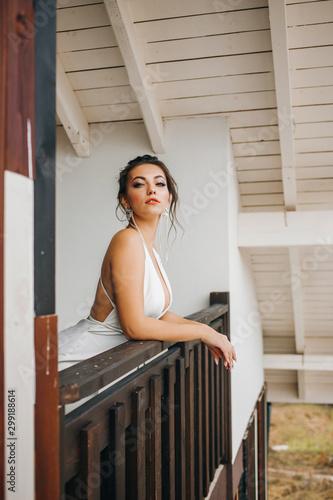 Beautiful girl in a white dress stands on the balcony looking outside
