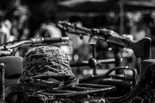 Military cap lying on old motorcycle with a rifle  toy  in the background. Black and white.