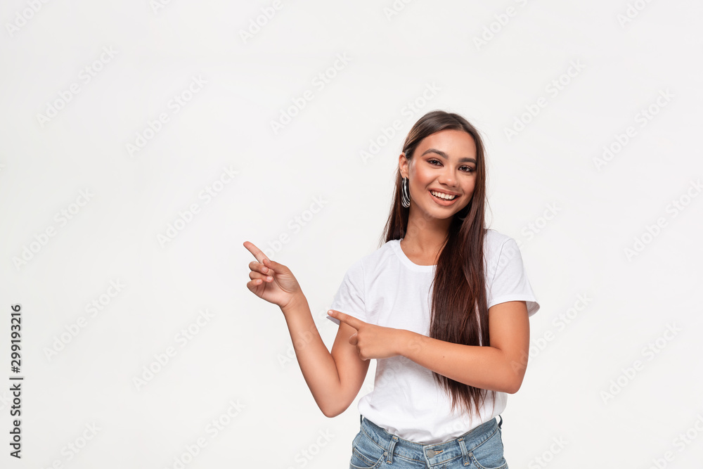 Pretty african-american teenager in a white t-shirt and blue jeans pointing at the empty space in a left side of a frame standing isolated over white background. Pretty african-american teenager in a white t-shirt and blue jeans pointing at the empty space in a left side of a frame standing isolated over white background.