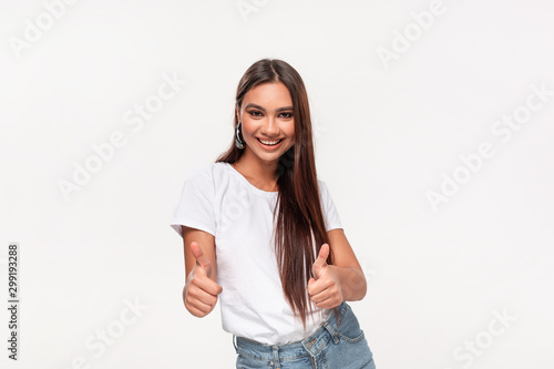 Excited pretty african-american teenager in a white t-shirt and blue jeans holding thumbs up  isolated over white background.