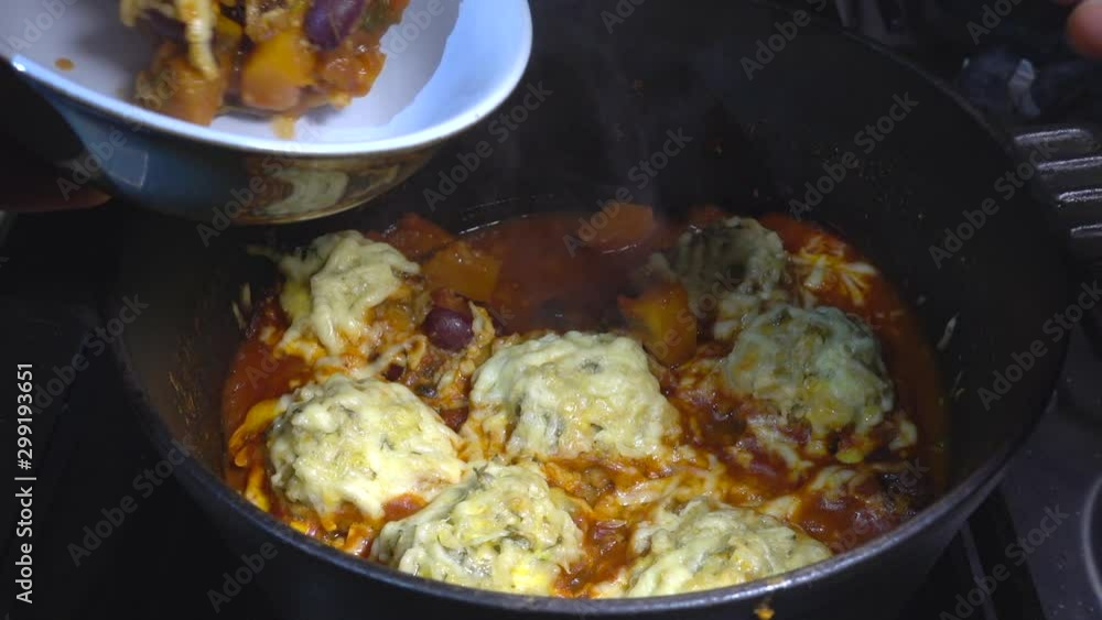 A slow motion close POV overhead shot of a man’s hand lifting a ladle of steaming, cheese topped dumplings and vegetable stew, from a cast iron cooking pot on a stove hob, and serving it into a bowl.. A slow motion close POV overhead shot of a man’s hand lifting a ladle of steaming, cheese topped dumplings and vegetable stew, from a cast iron cooking pot on a stove hob, and serving it into a bowl..