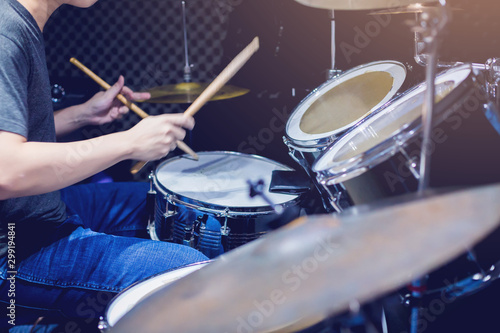 Young musicians wear t-shirts, jeans, and play the drum set and cymbals with wooden drumsticks in music room , the concept of musical instrument.