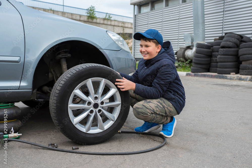 The boy helps at a car service. Replacing the wheels on the car, the jack holds the body in a raised position, with the wheel removed. The boy helps at a car service. Replacing the wheels on the car, the jack holds the body in a raised position, with the wheel removed.
