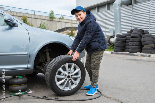 Children's auto mechanic changes the wheel on a car. Replacing wheels on a car. © Andrii