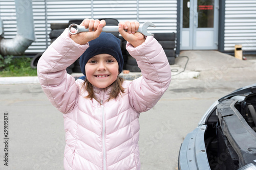 Portrait of a happy little girl with a wrench on the background of the garage. Auto repair concept. photo