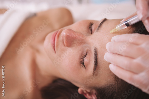 Close up of a woman getting anti-wrinkle filler injections in her forehead. Female client receiving skin firming injections by cosmetologist. Anti aging concept