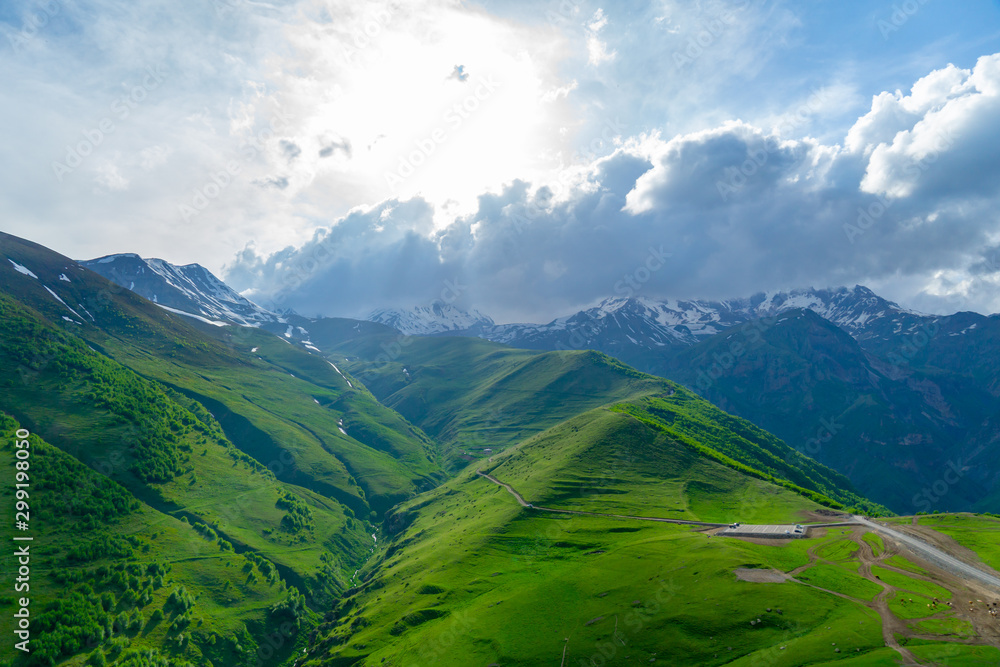 Landscape mountain view peaks in snow and green hills, deep blue sky and huge white clouds background, Caucasian mountains, Kazbek mountain Landscape mountain view peaks in snow and green hills, deep blue sky and huge white clouds background, Caucasian mountains, Kazbek mountain