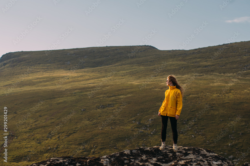 Girl in yellow jacket staying in mountains and looking to fjord