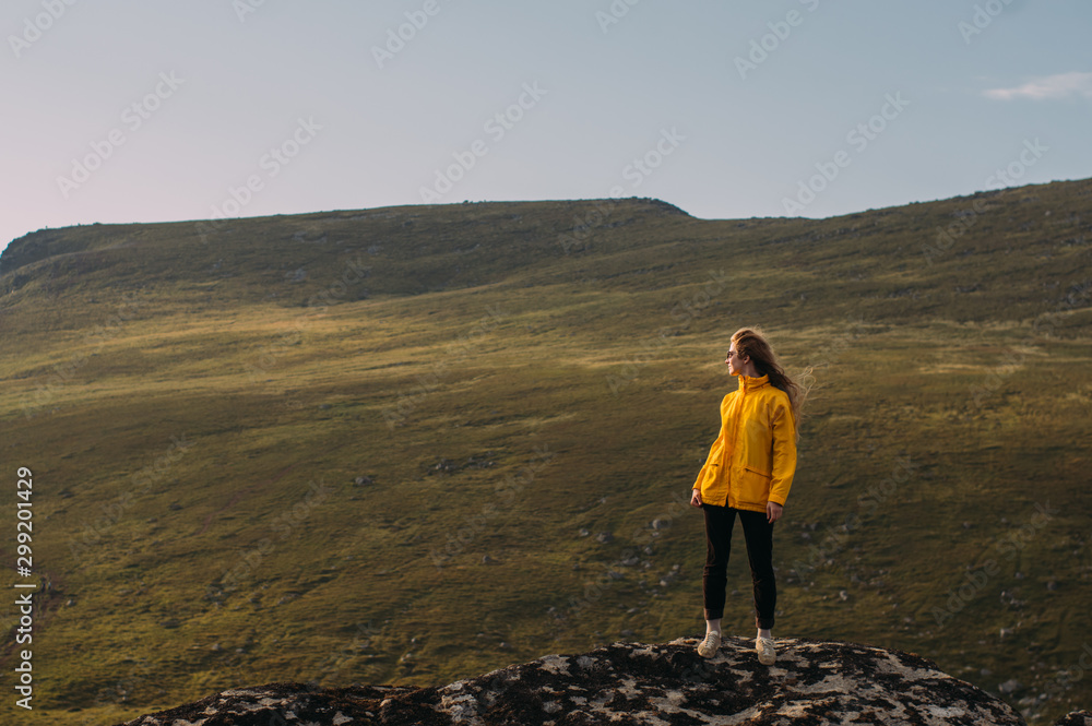 Fototapeta premium Girl in yellow jacket staying in mountains and looking to fjord