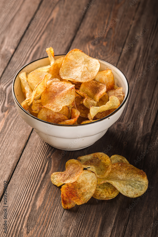 Handmade crispy potato chips in clay plate on wooden background Handmade crispy potato chips in clay plate on wooden background
