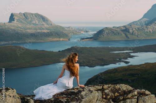Back of girl in wedding dress sitting on rocks in mountains and looking to fjord © el_caro