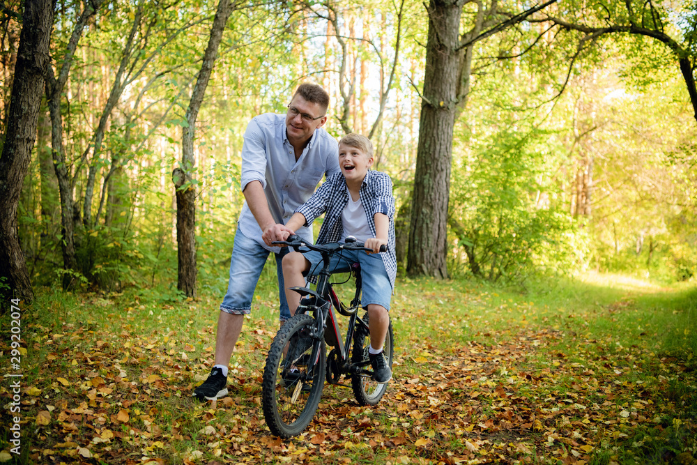 Naklejka premium Excited father and his son having fun together at the green park, teaching son how to ride a bicycle