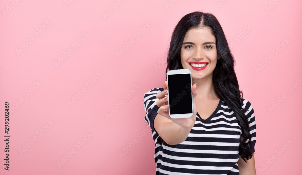 Young woman holding out a cellphone in her hand on a pink background Young woman holding out a cellphone in her hand on a pink background