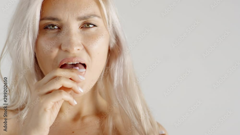 Close-up slow motion shot of young Caucasian blonde woman with bare shoulders putting two tabs of gum on tongue in mouth and chewing, while staring sensually Close-up slow motion shot of young Caucasian blonde woman with bare shoulders putting two tabs of gum on tongue in mouth and chewing, while staring sensually