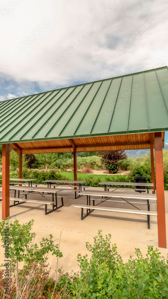 Vertical frame Cozy pavilion with green roof at a scenic park with blue sky and clouds overhead