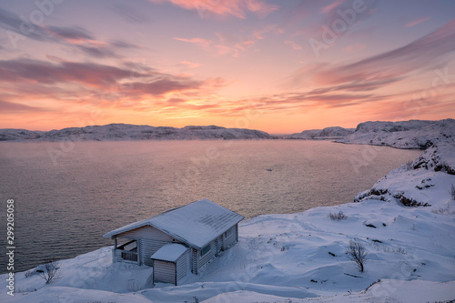 Wooden house and Barents sea at sunset in Teriberka, Murmansk Region, Kola Peninsula. Russia. It is not noise - Strong fog or smoke over sea. The sea is breathing in cold temperature. Focus on house