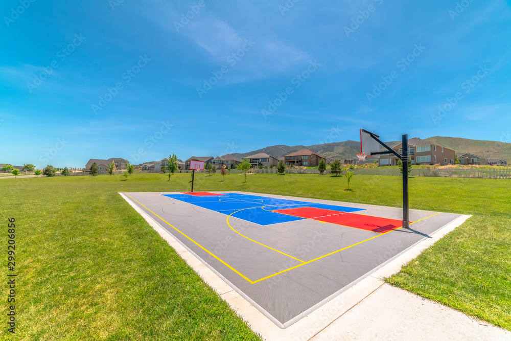Obraz premium Basketball court at a park against houses and buildings viewed on a sunny day