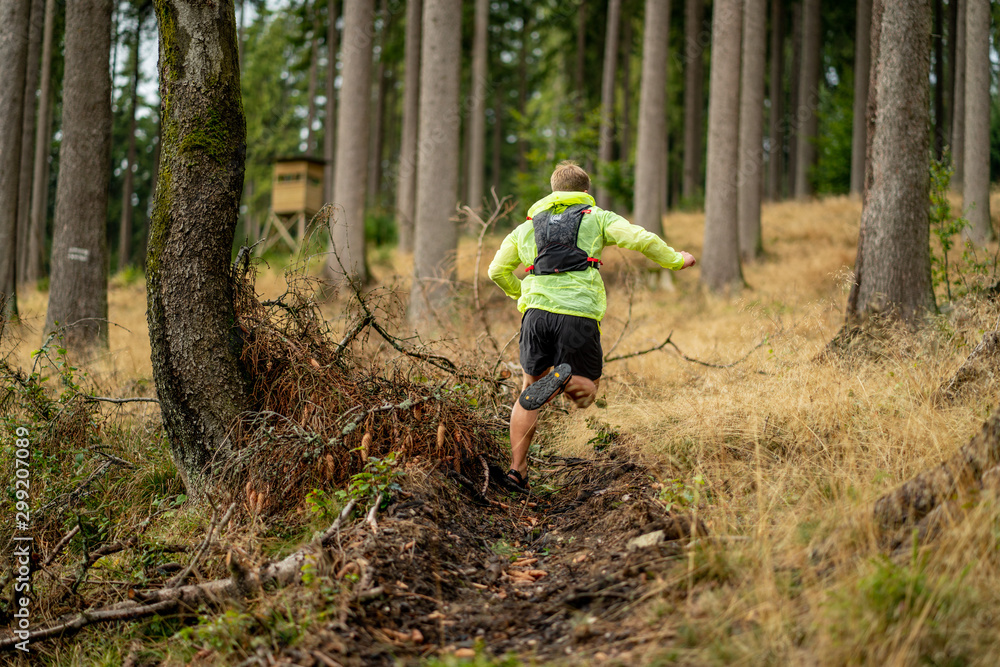 Young athlete runs uphill with a drinking backpack. Trail run in a beautiful autumn forest Young athlete runs uphill with a drinking backpack. Trail run in a beautiful autumn forest