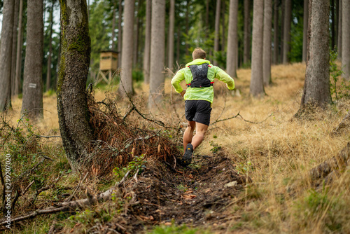 Young athlete runs uphill with a drinking backpack. Trail run in a beautiful autumn forest