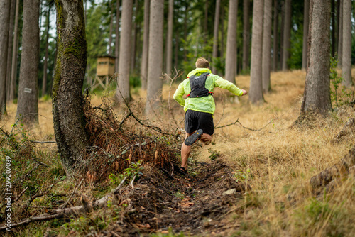 Young athlete runs uphill with a drinking backpack. Trail run in a beautiful autumn forest