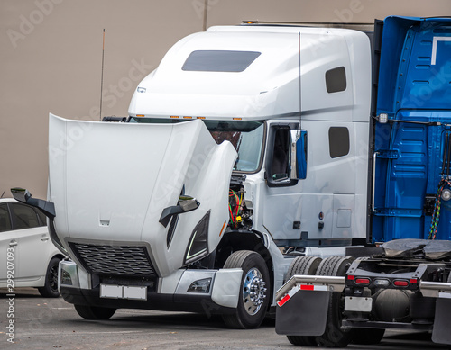 Big rig semi truck tractor standing on the parking lot with open hood for engine inspection and maintenance photo