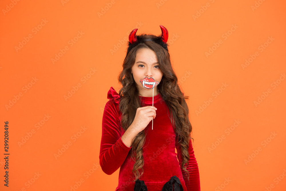 Vampires are real. Vamp girl. Little girl wear red devil horns and vampire teeth. Small girl with Halloween look. Halloween party girl orange background Vampires are real. Vamp girl. Little girl wear red devil horns and vampire teeth. Small girl with Halloween look. Halloween party girl orange background