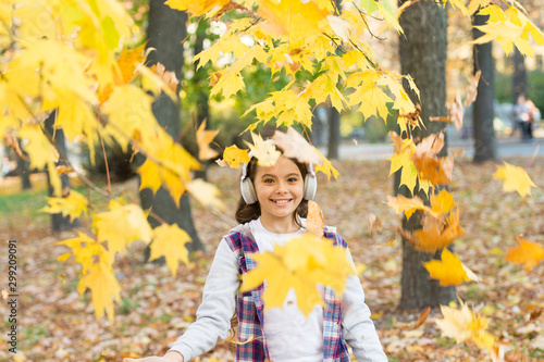 Melody of autumn. Falling leaves. Happy little girl wear headphones on autumn landscape. Cute child smile with stereo headphones. Small kid listening modern headphones. Headphones technology