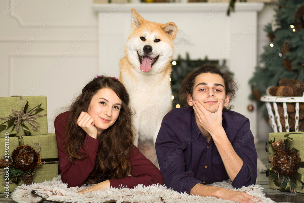 Young happy couple cuddling adorable akita inu dog with on the floor for Christmas holidays at home.