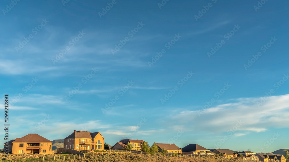 Panorama Blue sky and clouds over houses and grass covered hill viewed on a sunny day