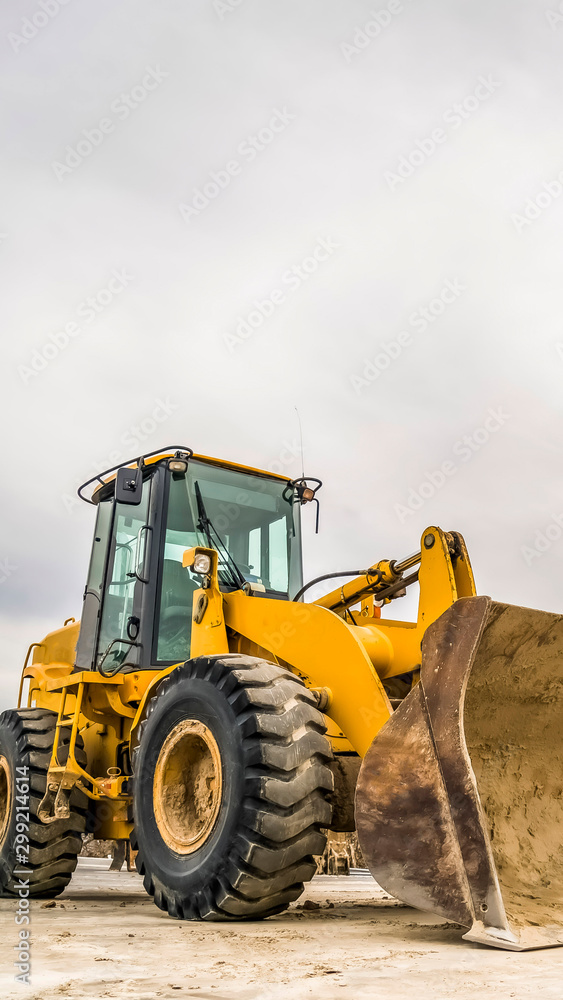 Vertical Front of a yellow bulldozer with mound of soil and cloudy sky in the background