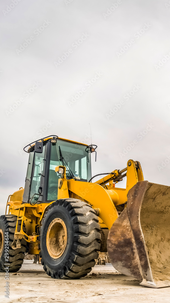 Vertical Front of a yellow bulldozer with mound of soil and cloudy sky in the background Vertical Front of a yellow bulldozer with mound of soil and cloudy sky in the background