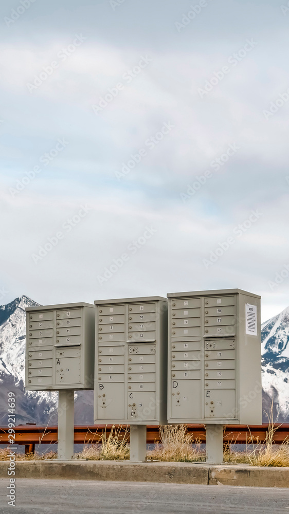 Obraz premium Vertical frame Selective focus mailboxes beside a road against snowy mountain and cloudy sky