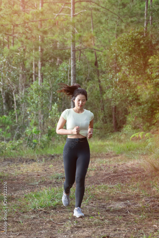 Young Asian woman wears sport black leggings runs on rural road in tropical  rain forest in