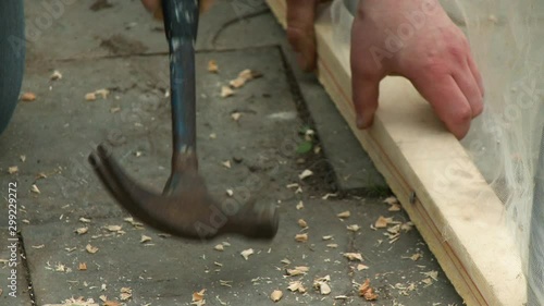 Handheld, medium close up shot of a person hammering a nail into a 2 x 4, securing a net around the lumber.