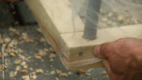 Handheld, medium close up shot of a person hammering a nail into a wooden post, securing a net around the wood.