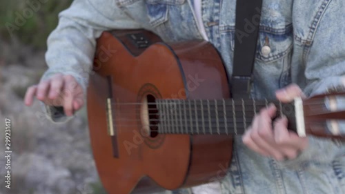 Chopped shot of the guitar mast while a man plays it with a denim jacket, detail of the strings and the frets while ripping with his hand photo