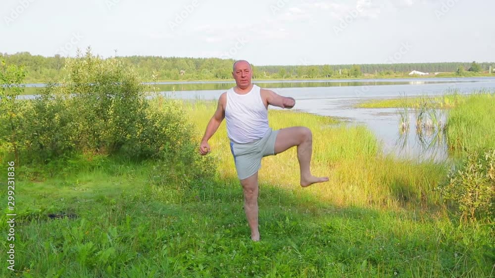 An elderly man does physical exercises on his feet on the lake shore in the morning. An elderly man does physical exercises on his feet on the lake shore in the morning.