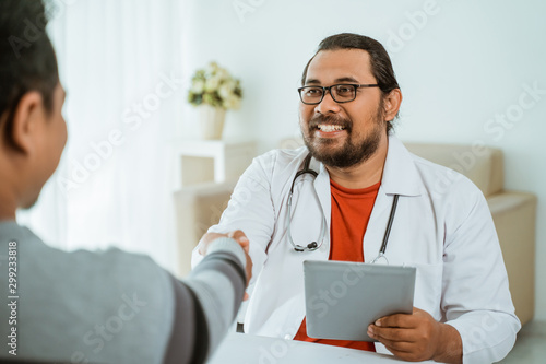 portrait of smiling doctor shaking hand with patient in his office