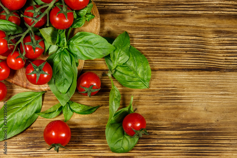 Fresh cherry tomatoes with green basil leaves on a wooden table. Top view Fresh cherry tomatoes with green basil leaves on a wooden table. Top view