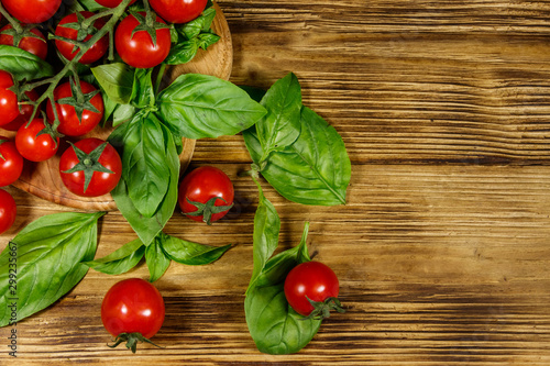 Fresh cherry tomatoes with green basil leaves on a wooden table. Top view