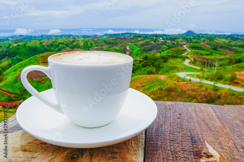 White hot coffee mugs placed on a wooden floor with green fresh mountain and morning fog as background