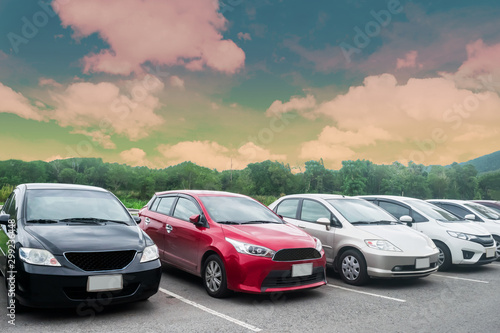 Cars parking in asphalt parking lot in a row with trees, colorful cloudy sky background in a park